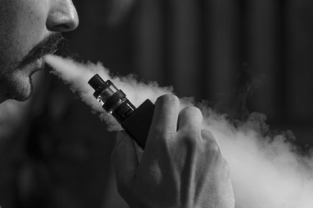 A man breathing out a stream of vapor while holding a vaping device.